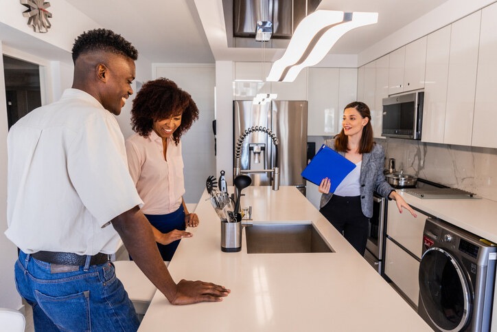 A professional woman explaining the features of a modern kitchen to a couple, demonstrating the role of property manager in condo units during a walkthrough or inspection.