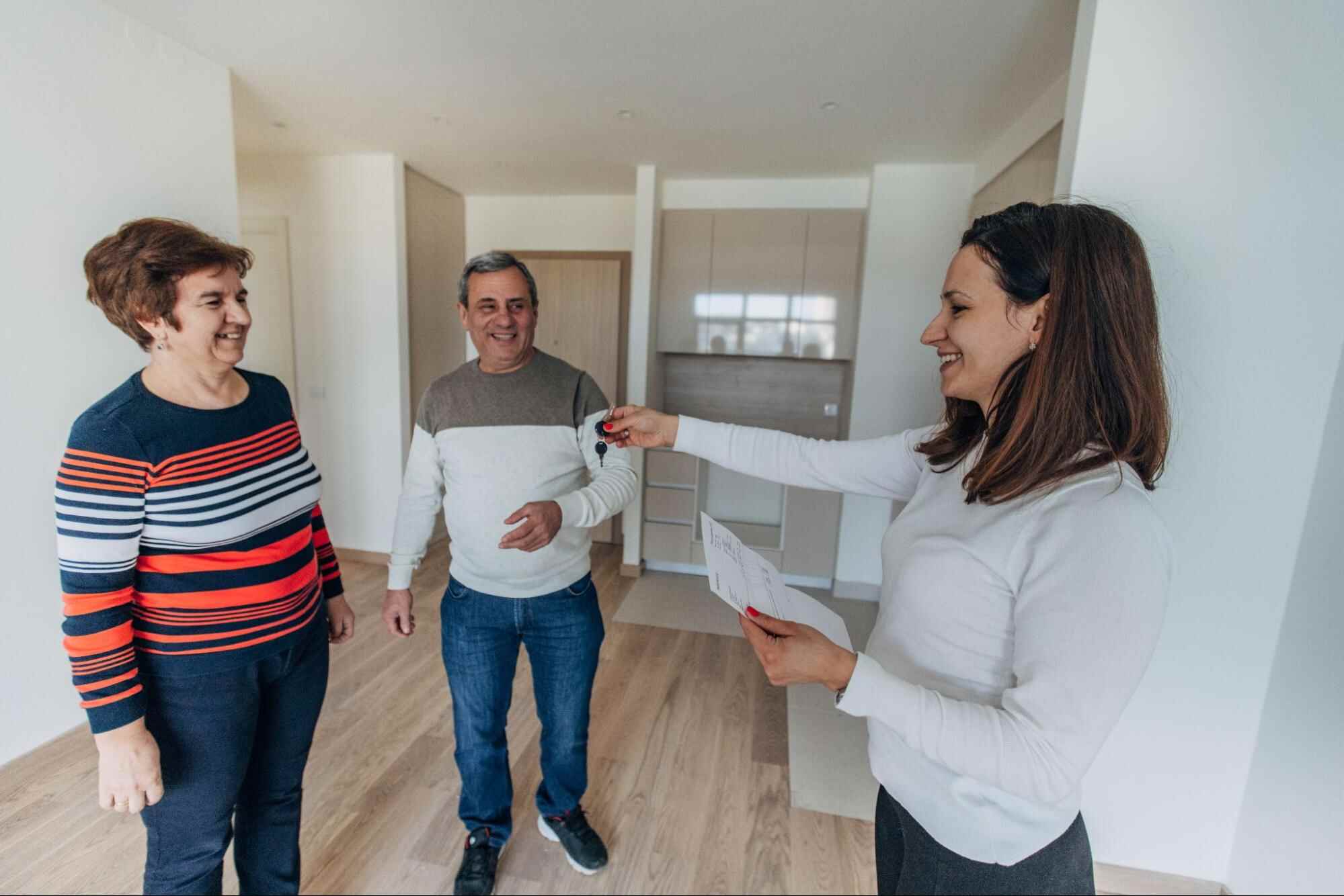 Property manager handing keys to new tenants inside a rental property while discussing the role of a leasing agent vs property manager.